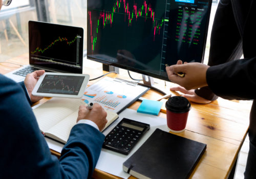 Bankers or asset managers managing investments with a tablet and two computers at a desk