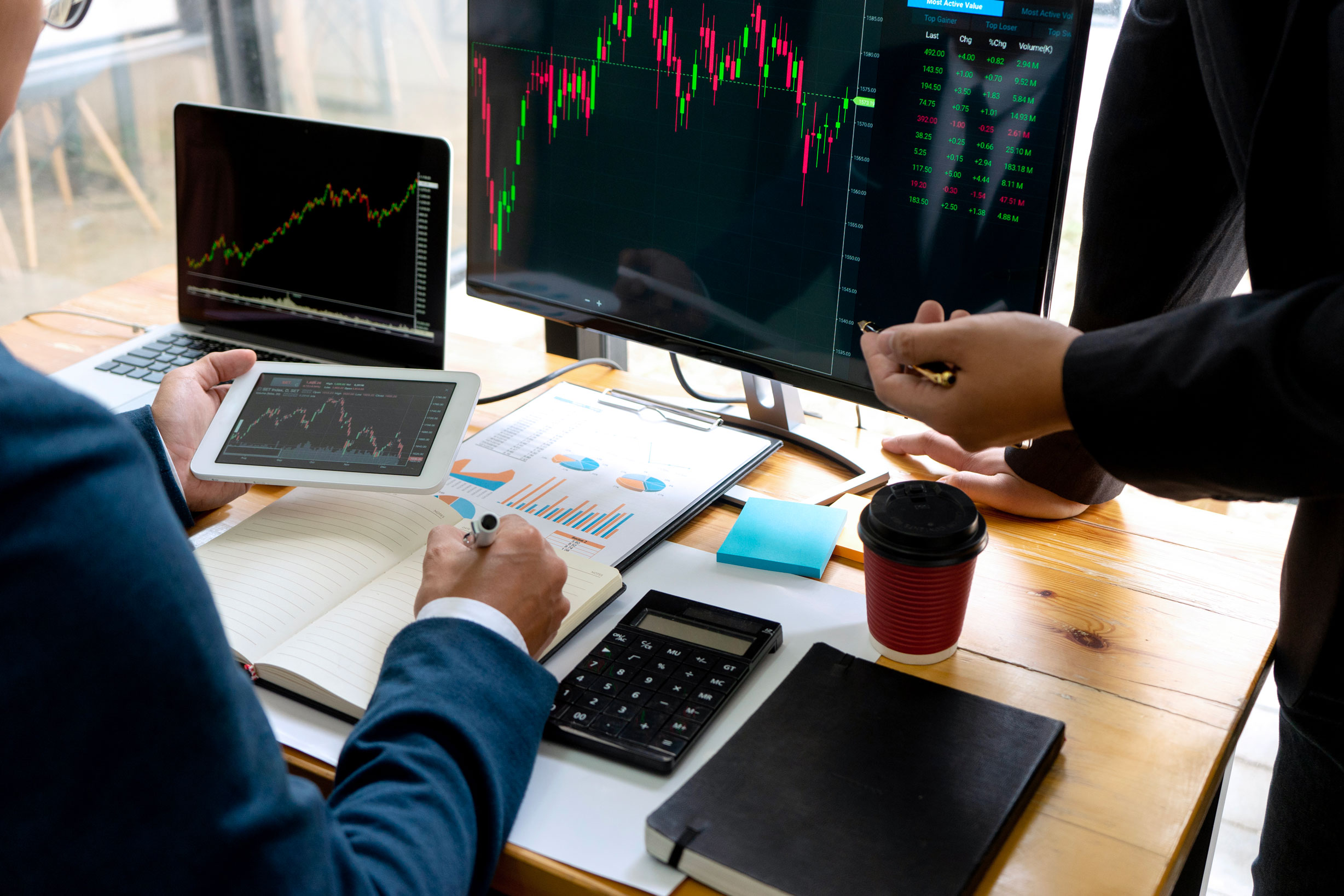 Bankers or asset managers managing investments with a tablet and two computers at a desk