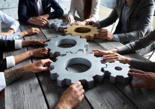 Hands of businesspeople managing a set of gears together, illustrating a collaborative dynamic towards a strategic goal in the tech era