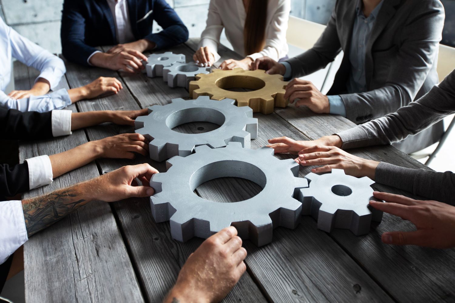 Hands of businesspeople managing a set of gears together, illustrating a collaborative dynamic towards a strategic goal in the tech era